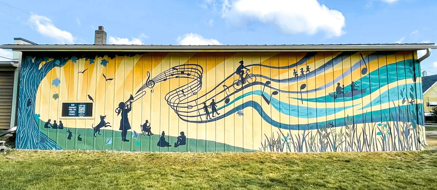 Wide view of the Revelry mural along the building, with music and community motifs in teal and gold.
