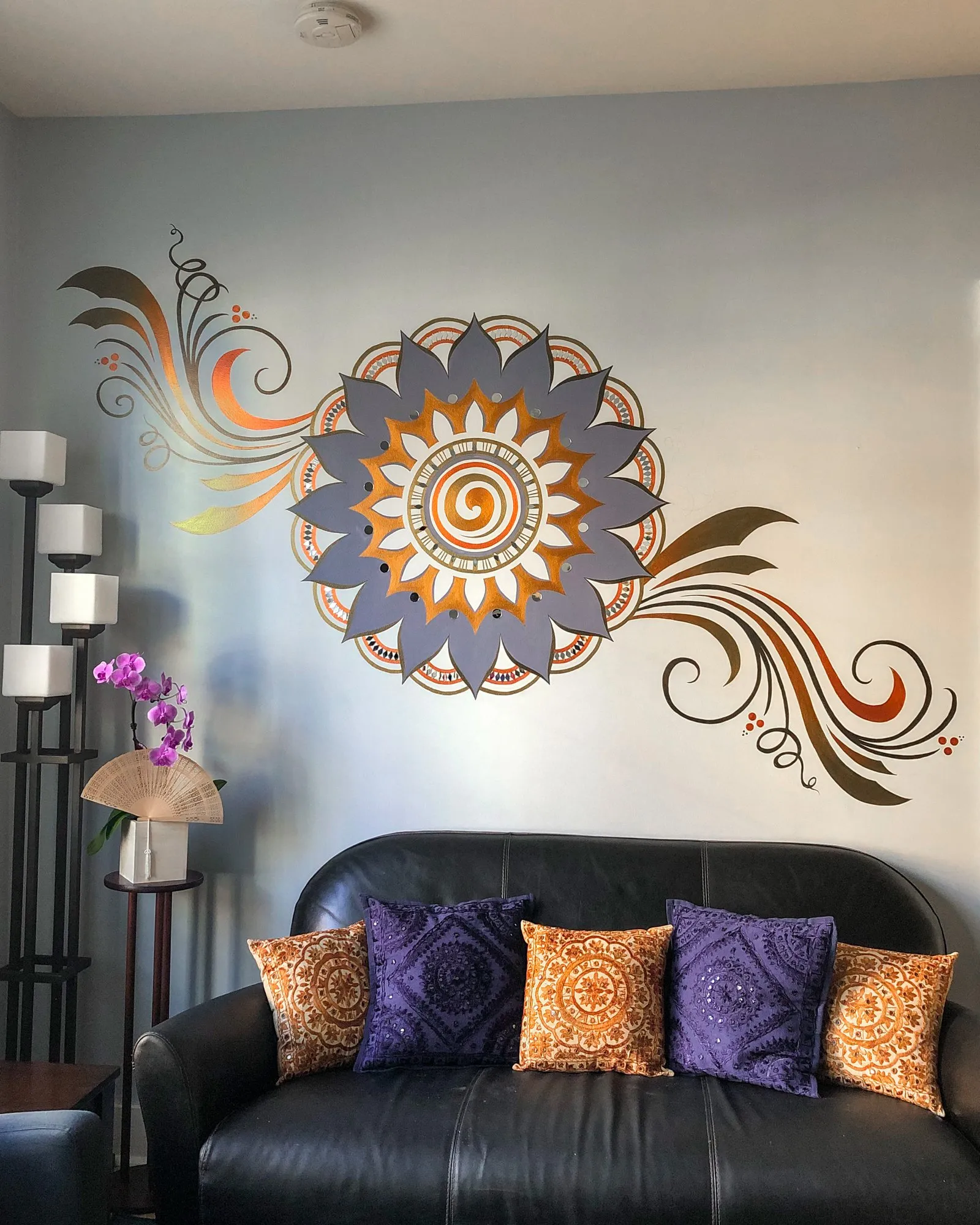 Metallic sunburst medallion with trailing scrollwork on a grey-blue living room wall above a dark sofa.
