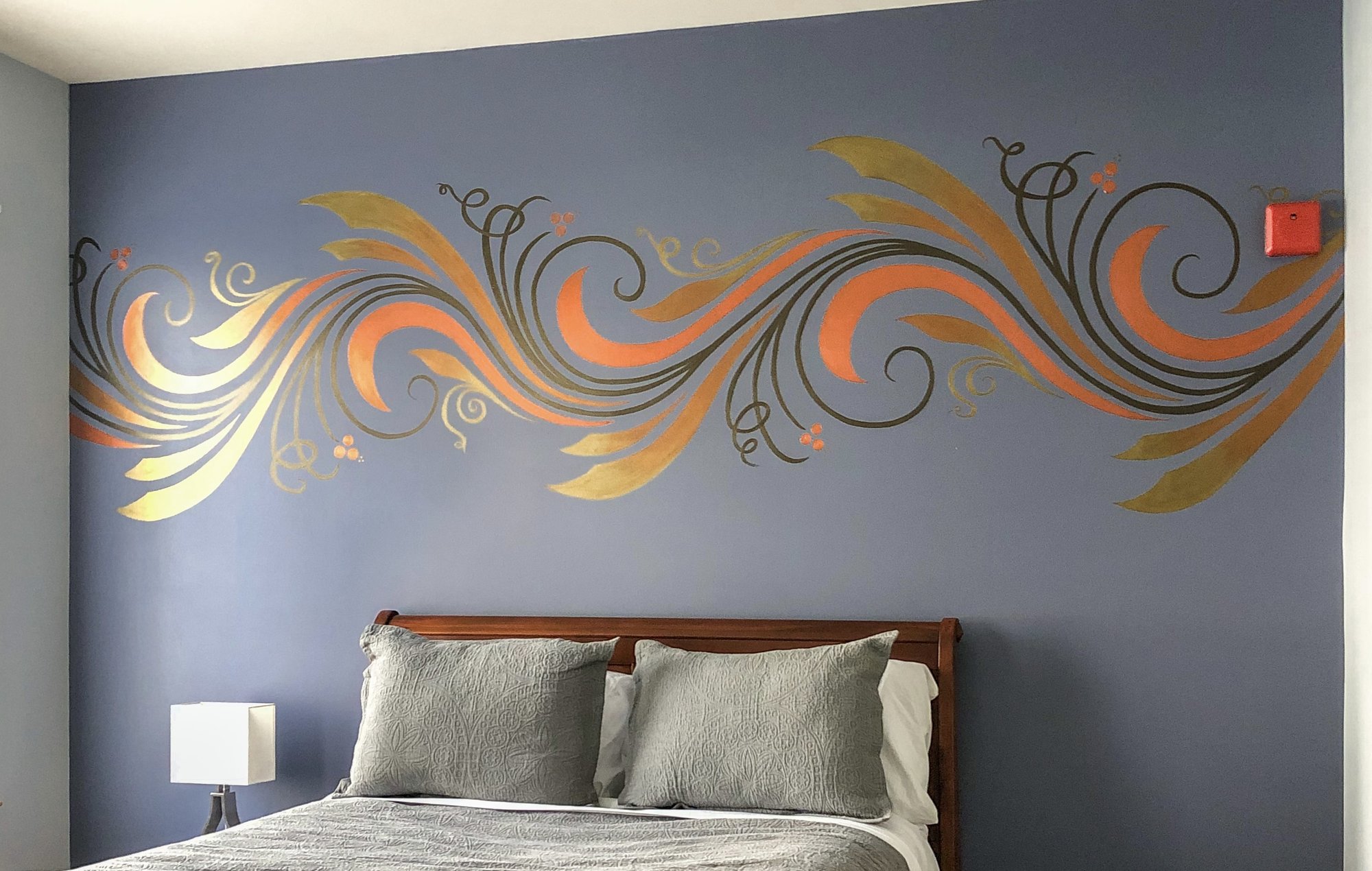 Metallic line-work mural flowing above a bed in copper and gold.