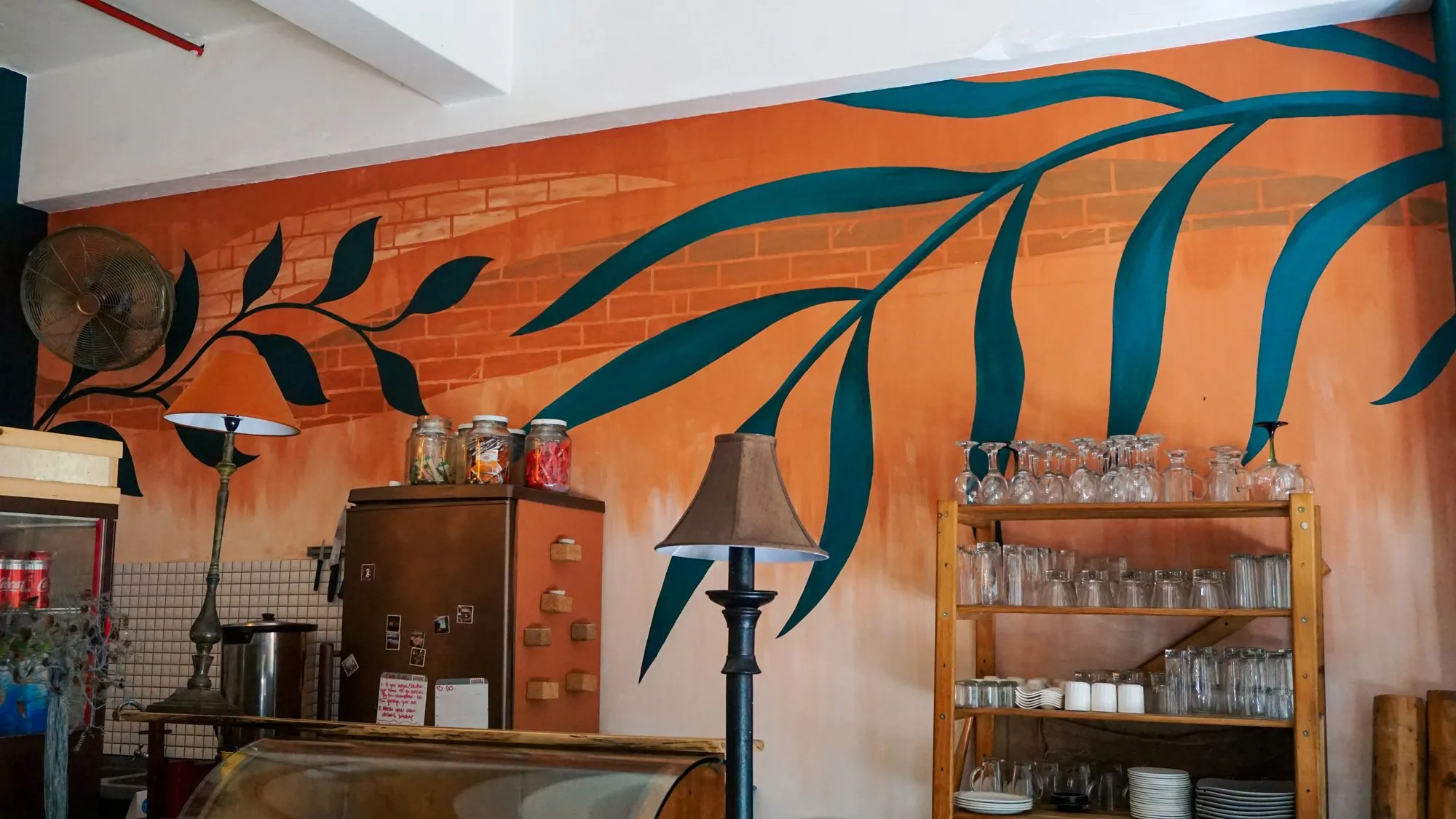 Teal eucalyptus mural running along the ochre cafe wall above the service counter.