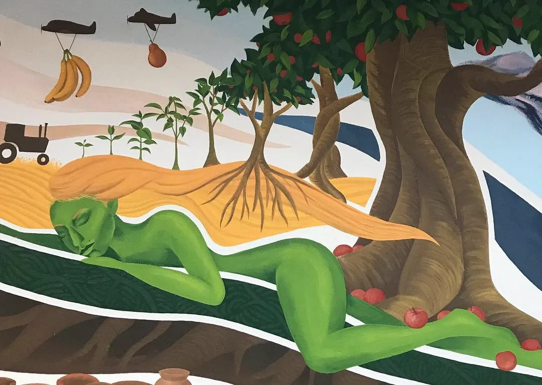 Reclining earth goddess with golden hair flowing into a wheat field, beside an apple tree as planes carry fruit away overhead