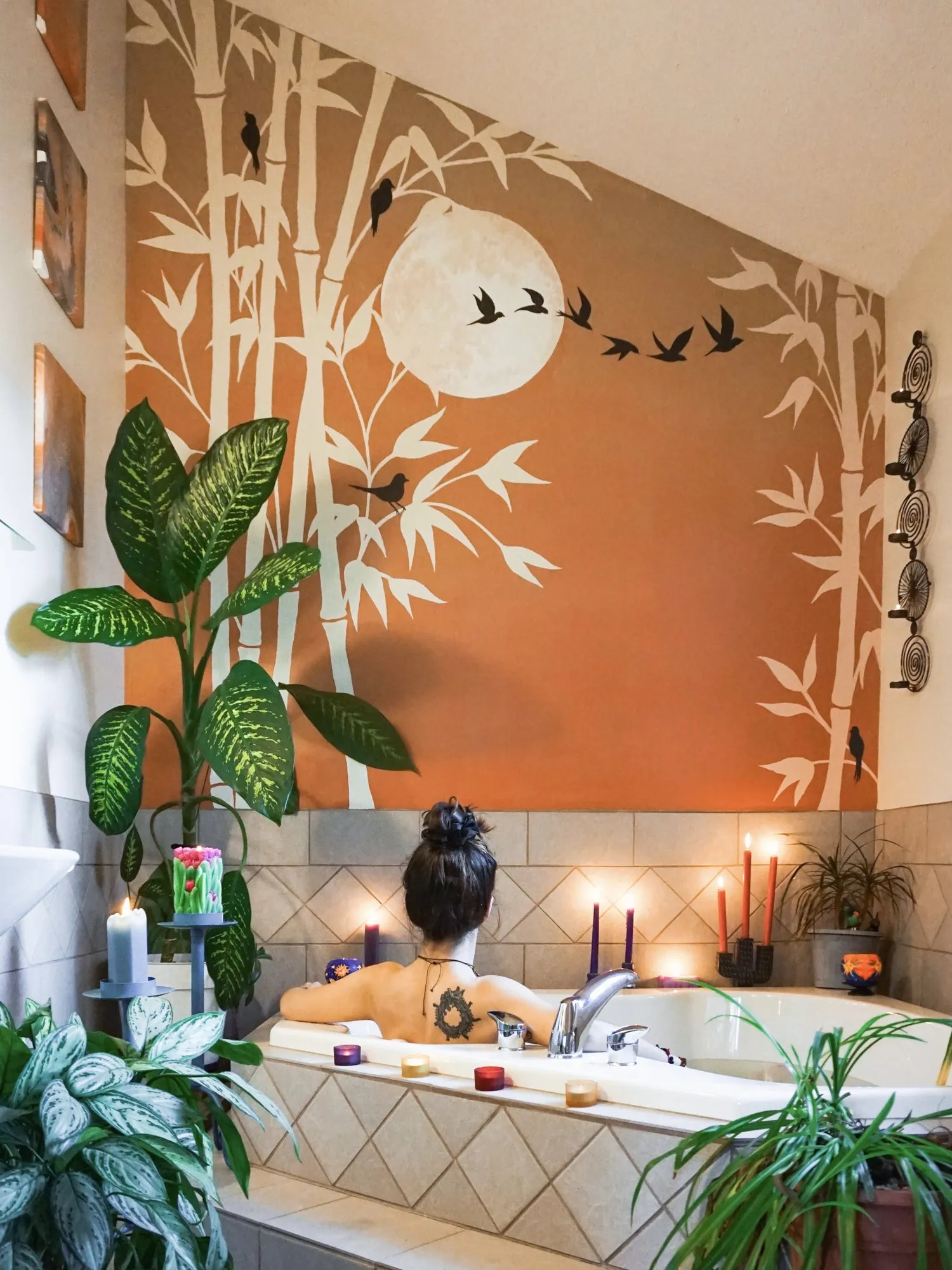 The Oasis bamboo and moon mural above a candlelit corner tub.