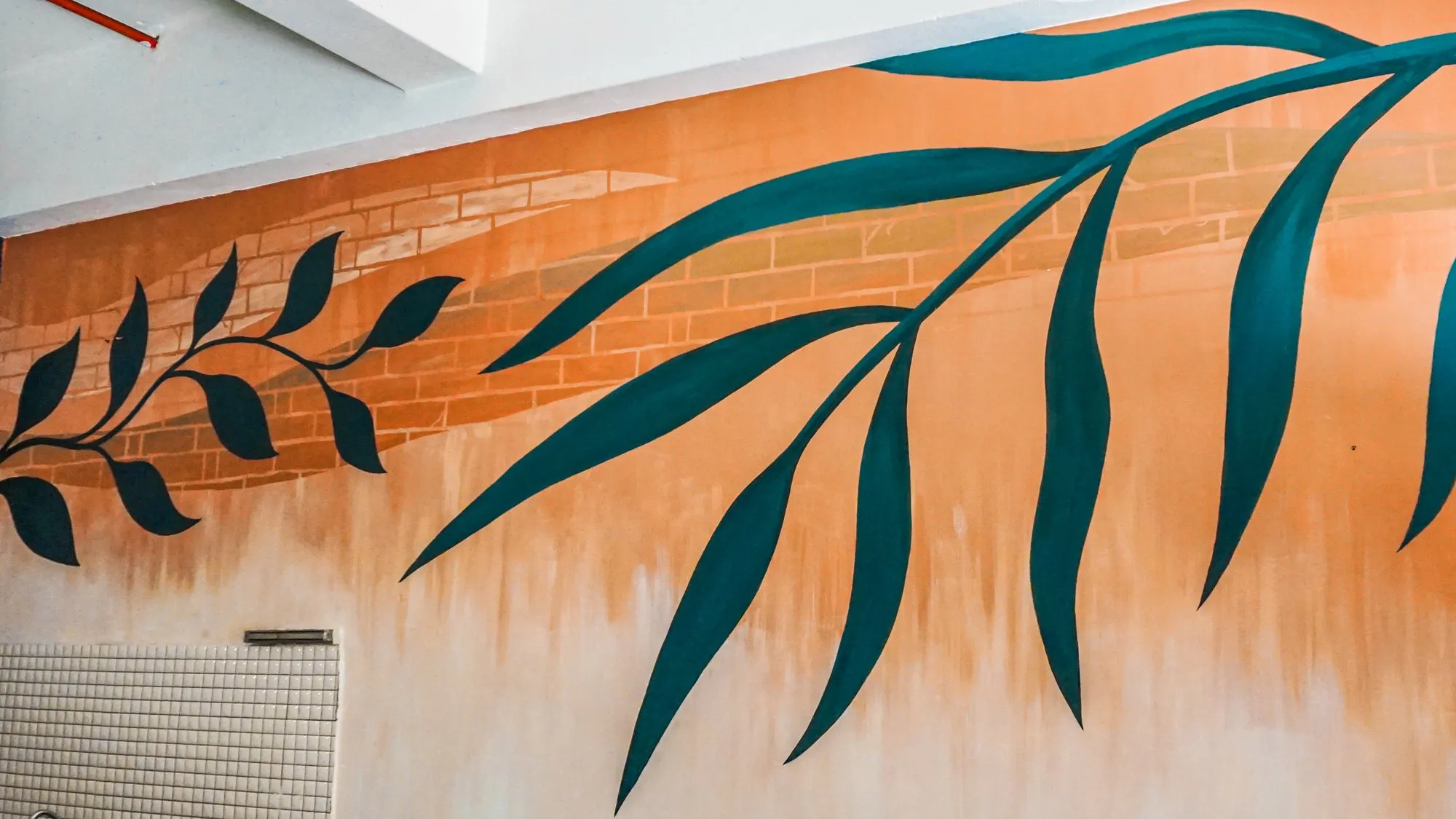 Trailing teal eucalyptus branches painted across an orange brick-and-plaster wall inside the cafe.