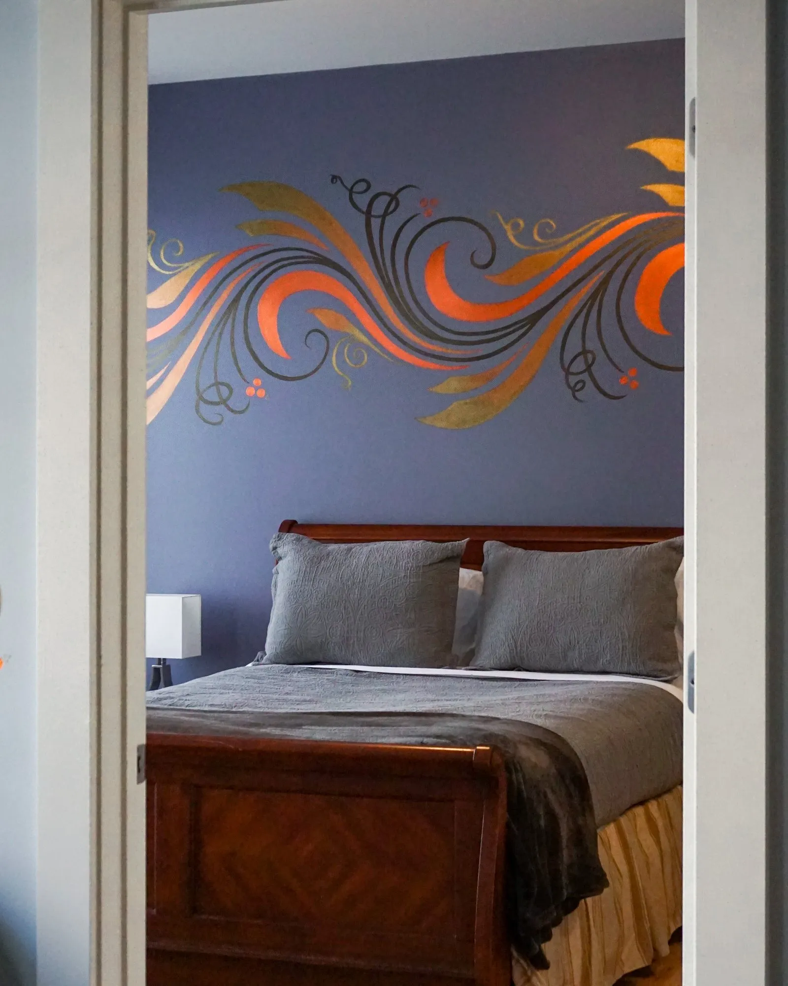 Scrollwork mural on a blue bedroom wall, seen through a doorway.