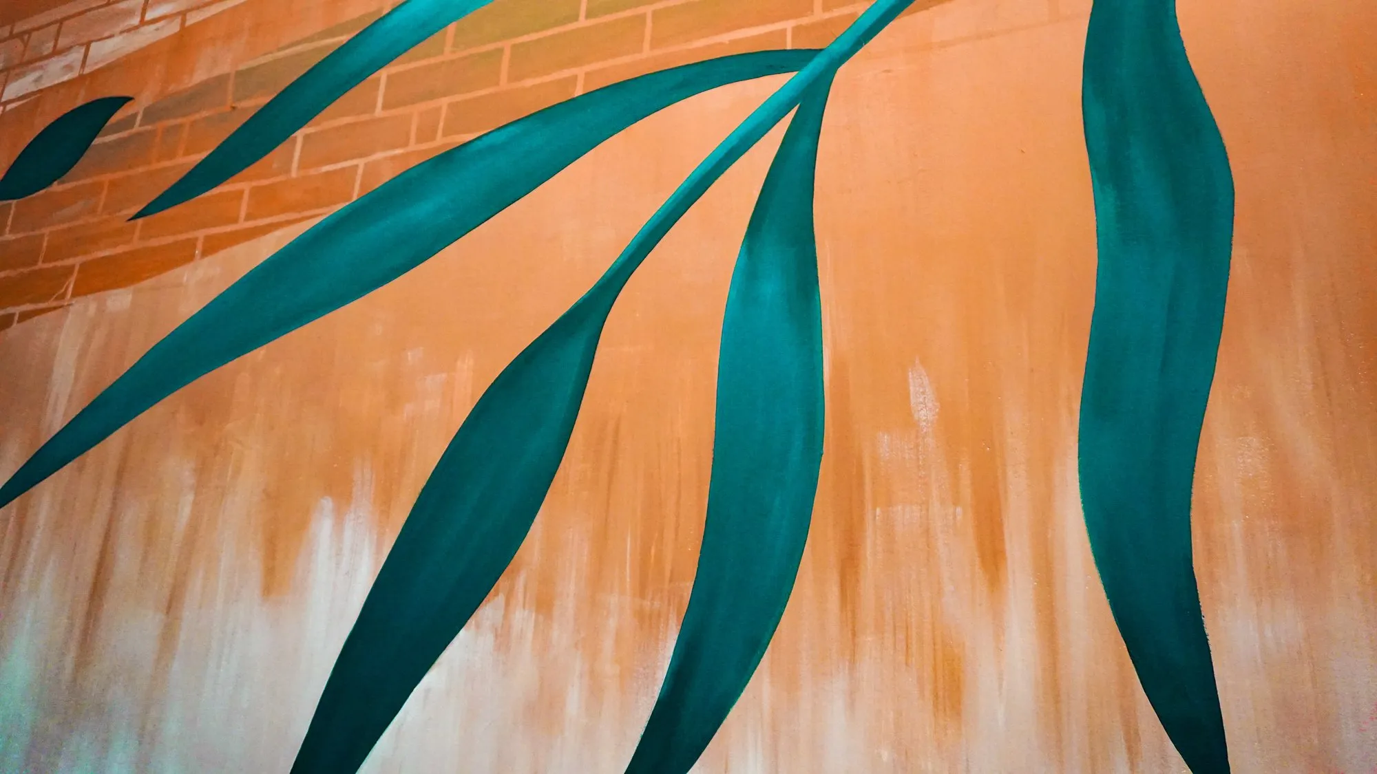 Detail of the teal botanical mural leaves against the warm ochre cafe wall.