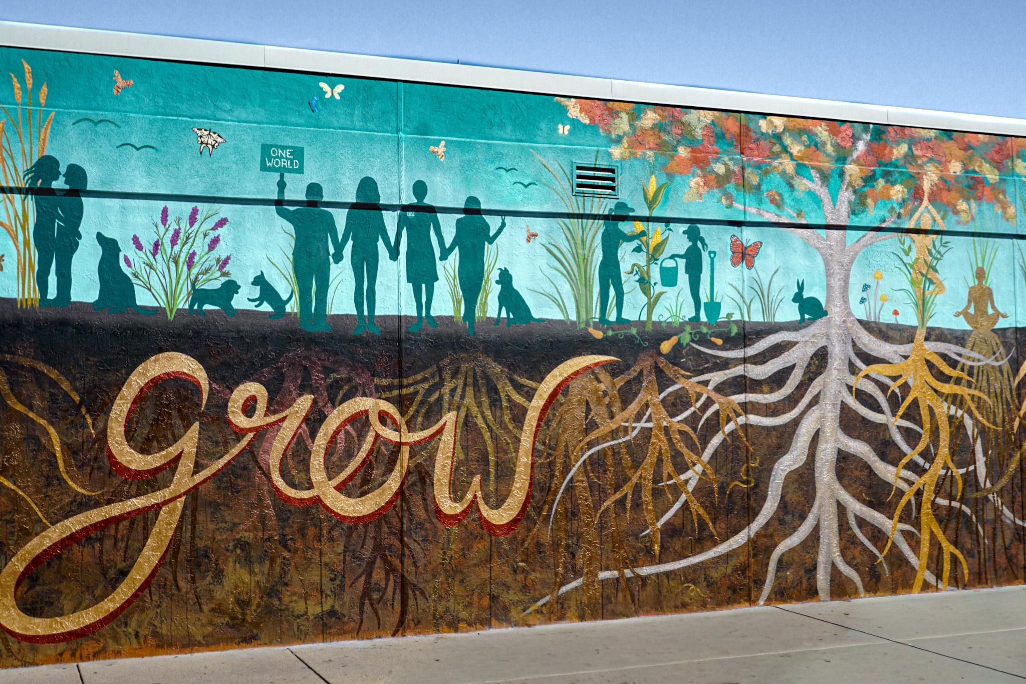 Community mural with a gold-leaf "grow" script, silhouetted figures, and white and gold root systems.