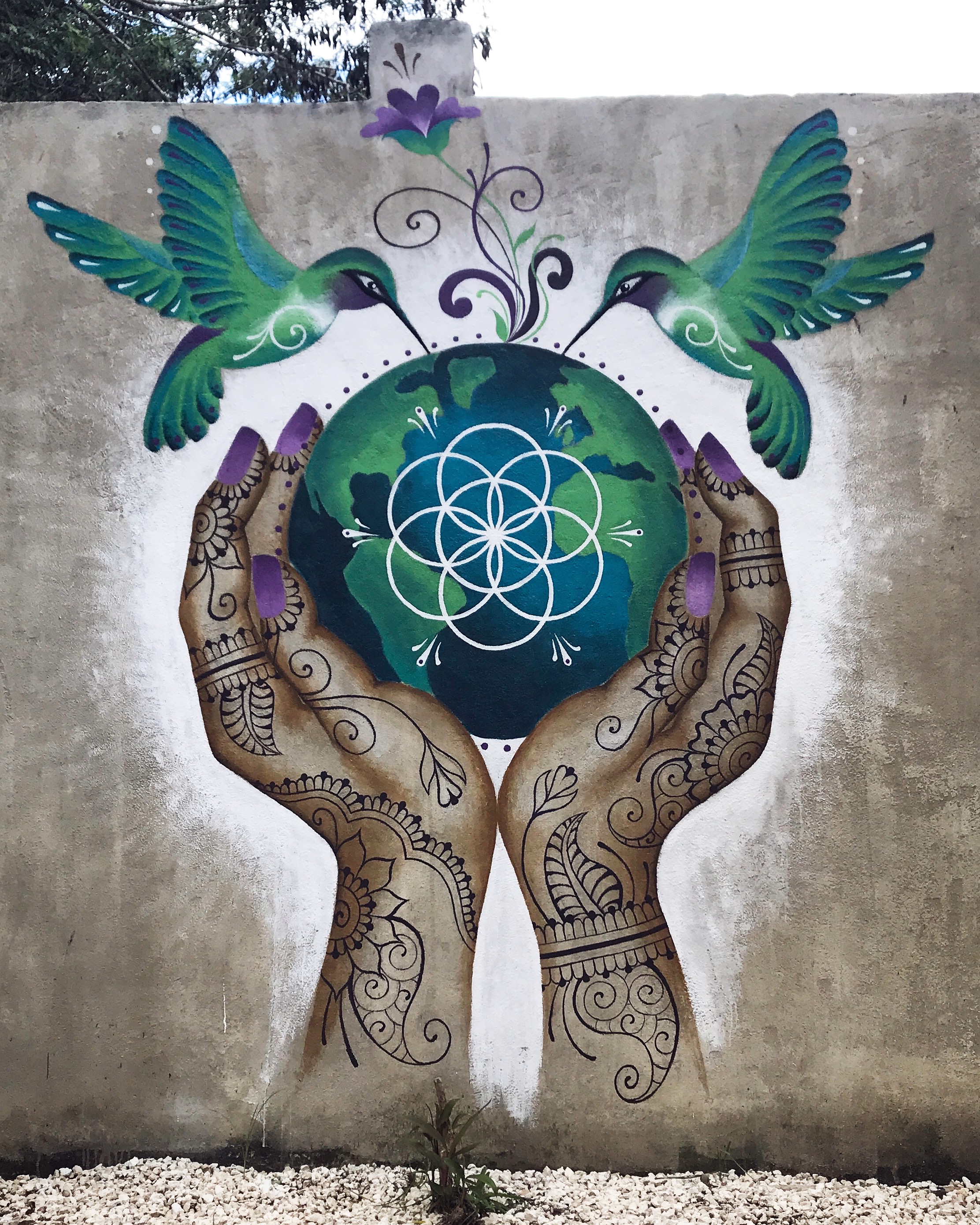 Mural of two hummingbirds and henna-patterned hands cradling the earth.