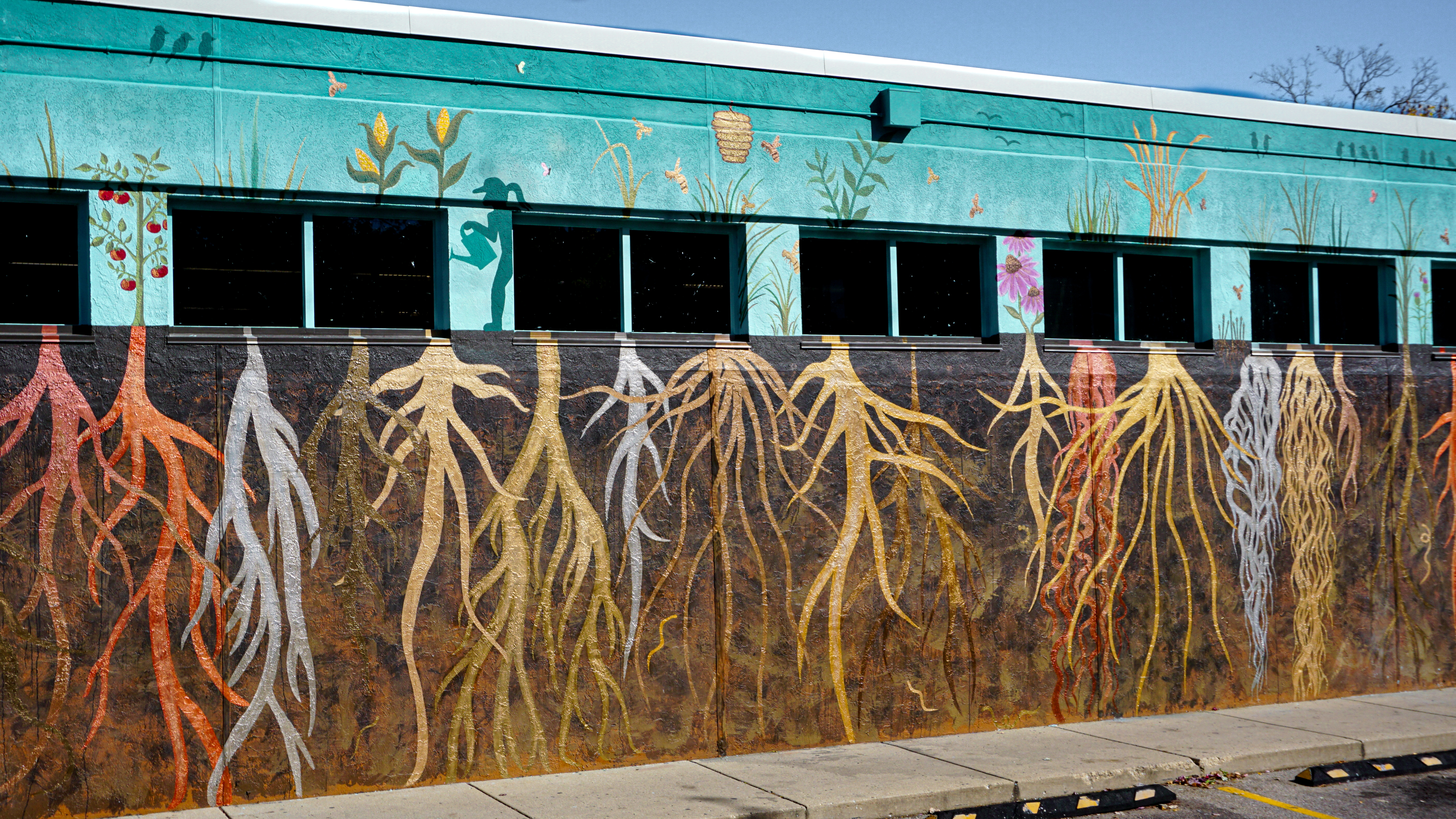 Roots of Our Community mural detail: a row of silhouetted figures above layered root systems on the lower wall.