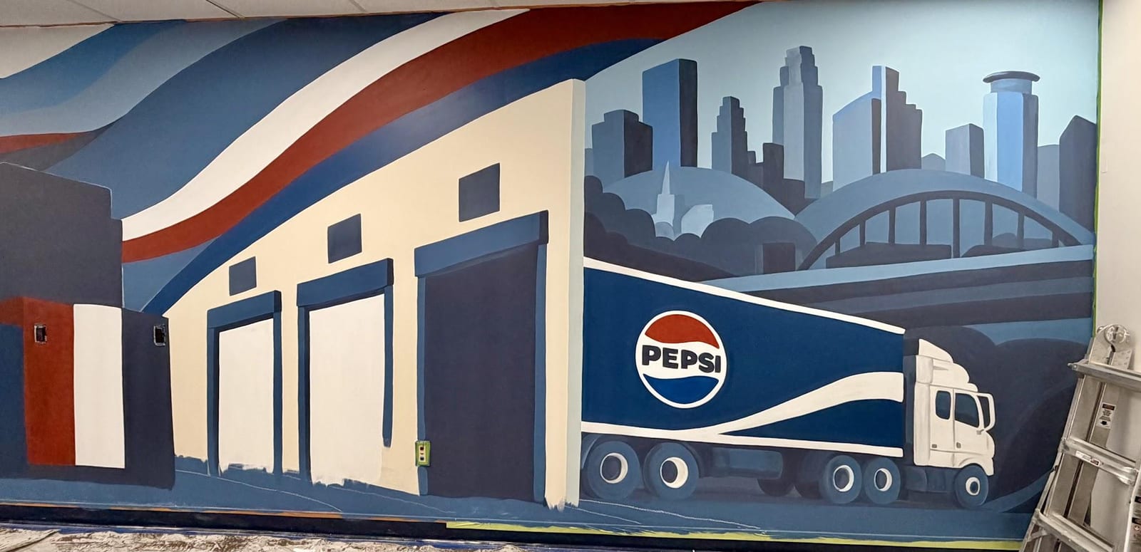 An in-progress wall showing a painted Pepsi semi trailer beside cream dock doors with the Minneapolis skyline and an arched bridge behind, a step ladder standing at the right edge of the wall and drop cloths across the floor.
